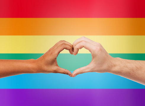 human hands showing heart shape over rainbow