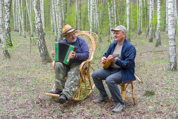 Two seniors playing music in birch forest