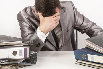 Hombre trabajando con la mano apoyada en la cabeza junto a un escritorio con carpetas. Vista de...