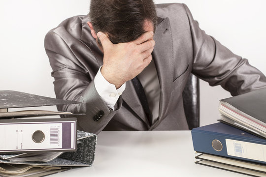 Hombre trabajando con la mano apoyada en la cabeza junto a un escritorio con carpetas. Vista de frente. Concepto: estr&eacute;s y preocupaci&oacute;n