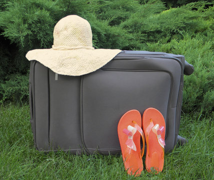 suitcase, sun hat, flip flops orange closeup on green background