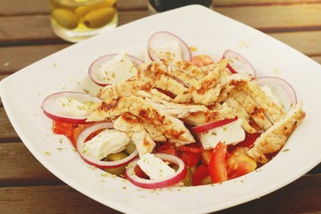 Greek salad with grilled turkey on wooden table
