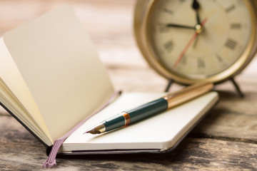 Open notebook with fountain pen and alarm clock
