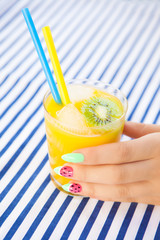 Hands close up of young woman with watermelon manicure holding glass of orange juice, manicure nail art concept 