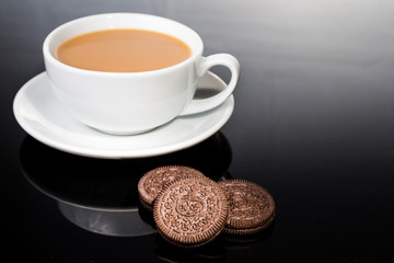 Creme-filled sandwich cookies and milk coffee on dark reflective background