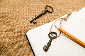 Opened notebook, keys and pencil on the old tissue
