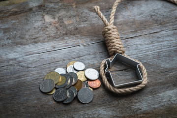 Hangman's noose with house and money on brown wooden surface