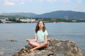 Fototapeta na wymiar little girl sitting on a rock by the sea and meditates