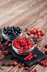 seasonal berries in a bowl on a wooden background. black currants, red currants, gooseberries. Copy space. free text space. close up
