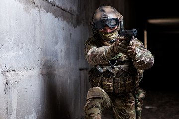 Armed ranger in camouflage aiming his gun in the dark room