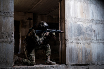 Soldier aiming a rifle in ruins/Armed soldier in camouflage, mask and helmet aiming a rifle in a dark room