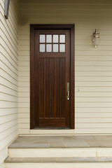 Skinny brown front door with white siding and modern porch light