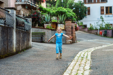 Fototapeta na wymiar Cute little girl running along the street in a small village