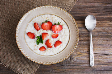 Oatmeal porridge with strawberries in plate on old wooden table