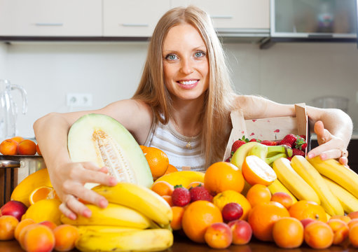 Happy blonde young woman with heap of fruits