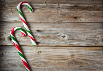 horizontal image of an old rustic wood background with two large candy canes placed side by side on one side of the image great for a greeting card idea,