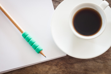 Pencil on open blank notebook with coffee cup