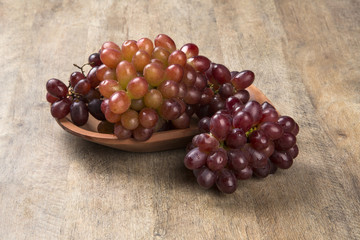 Some red grapes in a wooden pot over a wooden surface seen from