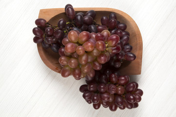 Some red grapes in a wooden pot over a wooden surface seen from