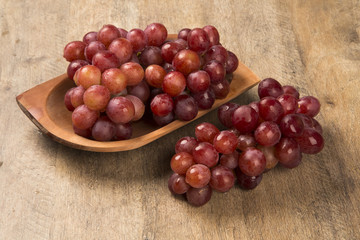 Some red grapes in a wooden pot over a wooden surface seen from