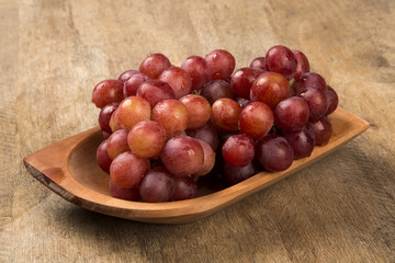 Some red grapes in a wooden pot over a wooden surface seen from