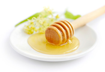 Honey dipper with honey with flowers of linden on white saucer