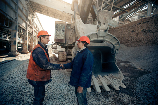Workers shaking hands near the excavator mine industry.