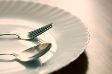 Fork and spoon with white plate on wooden table in a restaurant. Focus on fork.