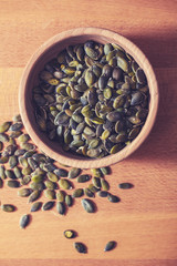 Dried pumpkin seeds in a bowl, on wooden background