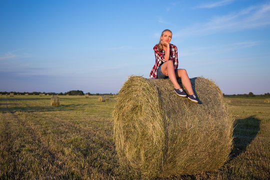 country concept - young woman sitting on haystack over blue sky