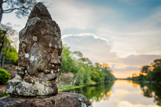 Mossy stone face Asura and sunset over moat in Angkor, Cambodia