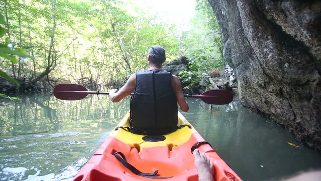 old man paddles on kayak in canyon among mangrove jungle	