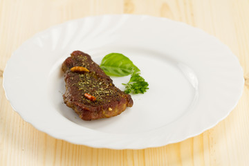 roast pork on white plate on wooden background with vegetables and herbs