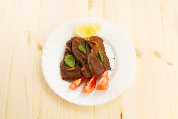 roast pork on white plate on wooden background with vegetables and herbs