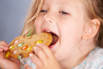 Naklejka premium Close Up Of Young Girl Sitting At Table Eating Cookie