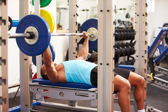 Young man bench pressing weights at a gym, side view