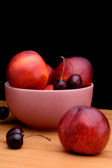 Fototapeta na wymiar Nectarines and cherries on a wooden table on a black background