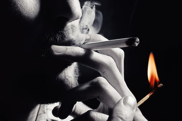Men's hand lights a cigarette with a match