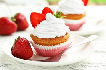 Tasty cupcake with fresh strawberry on white wooden background