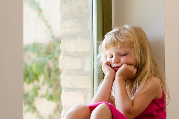 bored girl with long blond hair sitting by the window