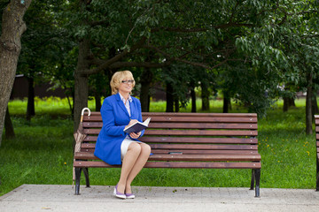 Mature business woman in a jacket with diary sitting on a bench