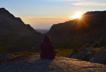 Young woman sitting on a mountain rock admiring the sunset