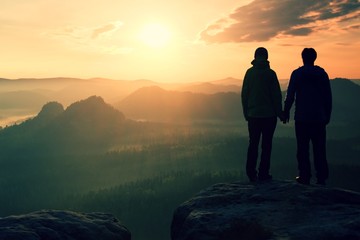Young pair of hikers hand in hand on the peak of rock empires park and watch over the misty and...