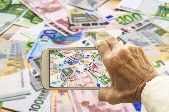 Old hand takes a picture of euro banknotes on smart phone.