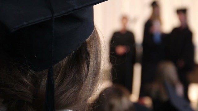 Girl in academic cap looking at students receiving diplomas, college graduation