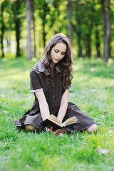 Schoolgirl reading a book sitting on the grass. Beautiful girl reading a book