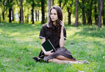 Schoolgirl reading a book sitting on the grass. Beautiful girl reading a book