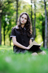 Schoolgirl reading a book sitting on the grass. Beautiful girl reading a book