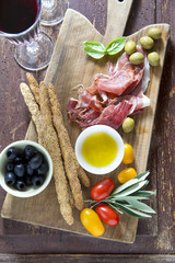 cured meat on a wooden cutting board with red tomatoes, olives a