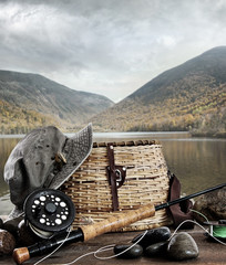 Fly rod with creel and equipment on wood - obrazy, fototapety, plakaty